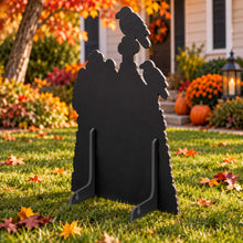 Load image into Gallery viewer, A black metal Halloween yard sign shaped like a tombstone with two crows perched on top, displayed on a green lawn in front of a house during autumn.