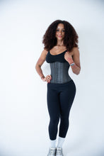 Load image into Gallery viewer, A woman stands against a plain light background wearing a dark gray compression waist trainer over a black top and black leggings.