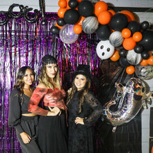 Load image into Gallery viewer, Three women posing in front of a Halloween-themed balloon arch with purple tinsel curtain.