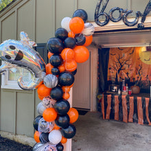 Load image into Gallery viewer, Halloween-themed balloon arch with a decorated garage door in the background
