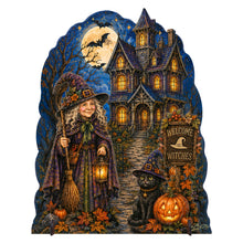 Load image into Gallery viewer, A Halloween-themed decorative cutout sign featuring a witch in a purple cloak holding a broom and lantern beside a black cat, pumpkins, autumn leaves, and a haunted house at night under a full moon. The sign is photographed on a plain white background.
